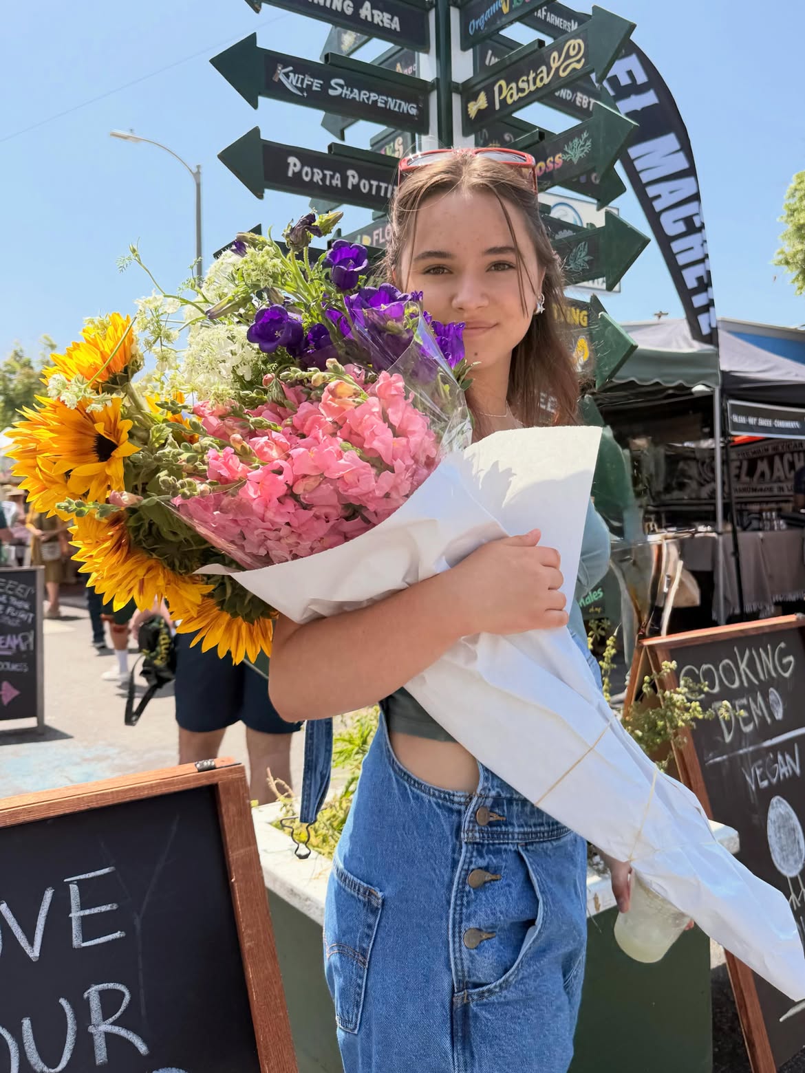 A young girl holding a large bouquet of colorful flowers at a farmers market