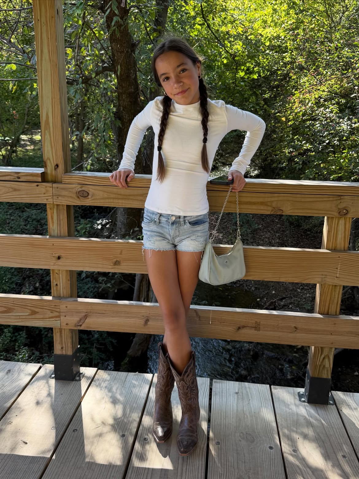 A young girl with braided hair standing on a wooden bridge